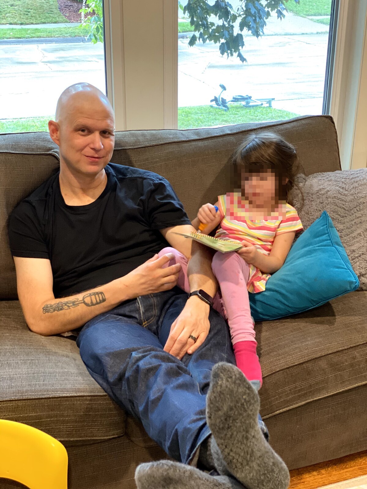 Clay Collins, bald from chemo, on the couch with one of his daughters