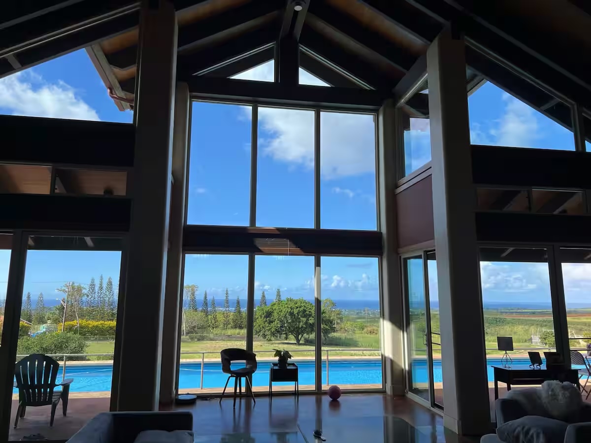 The great room at Kualapa, with floor-to-ceiling windows looking past the pool to the Pacific Ocean